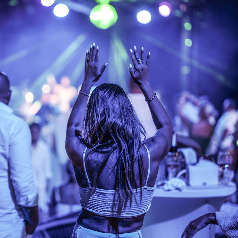 Woman with raised hands enjoying a concert with colorful stage lights at Falkensteiner Hotel Belgrade