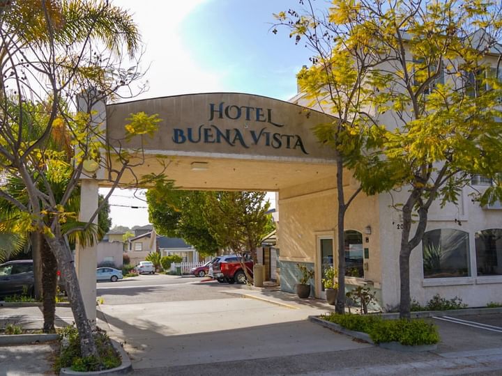 A hotel entrance with a sign reading 'Hotel Buena Vista', trees, and a parking lot.