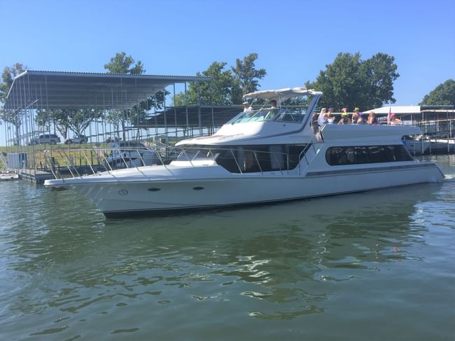 A large white multi-deck luxury yacht with passengers departs from a covered harbor at Shangri-La Resort and Golf Club