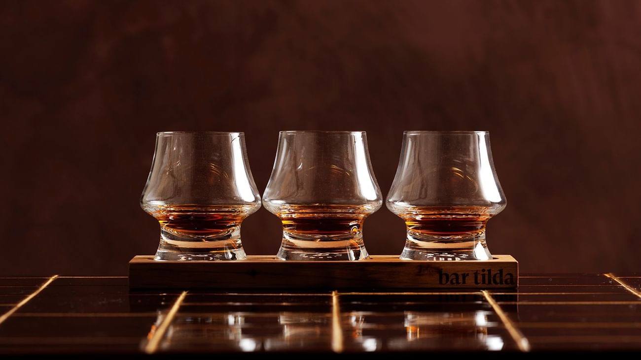 Three amber-colored glasses filled with liquid, arranged on a wooden stand labeled 