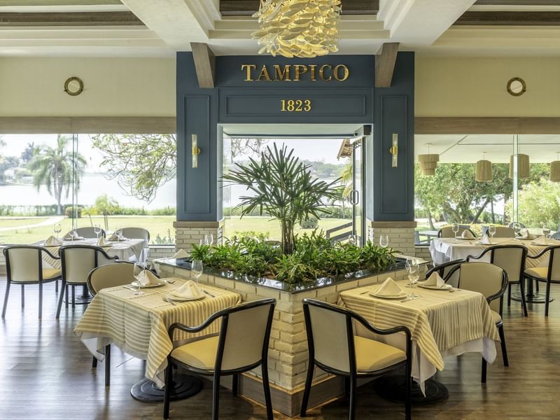 Restaurant with white dining tables, chairs and large windows with garden view at Fiesta Inn Tampico