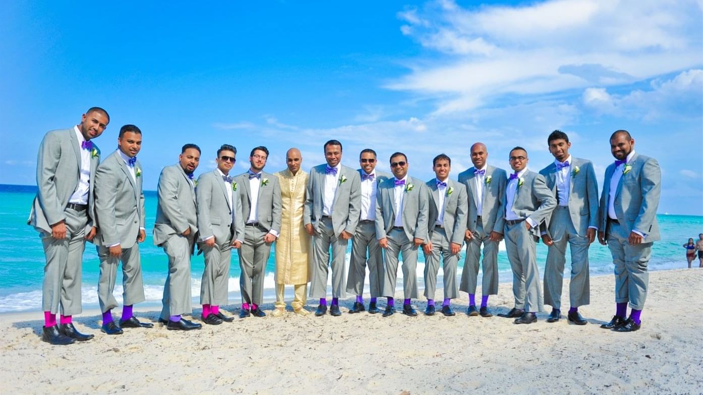 Groomsmen in stylish suits posing on a sandy beach at The Diplomat Resort