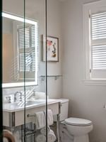 White vanity by a toilet under a window with wooden shutters in Corner King at Warwick Melrose Dallas