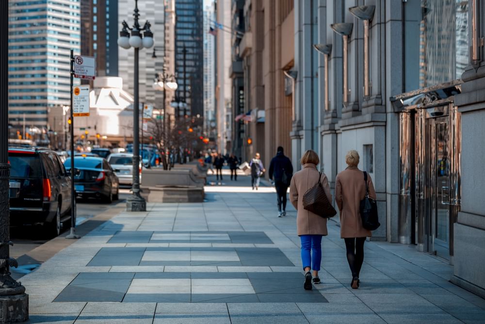 Two women in coats walk down a busy city sidewalk at Warwick Allerton Chicago