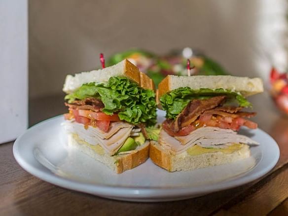 Two halves of a sandwich with lettuce, bacon, and avocado on a plate.