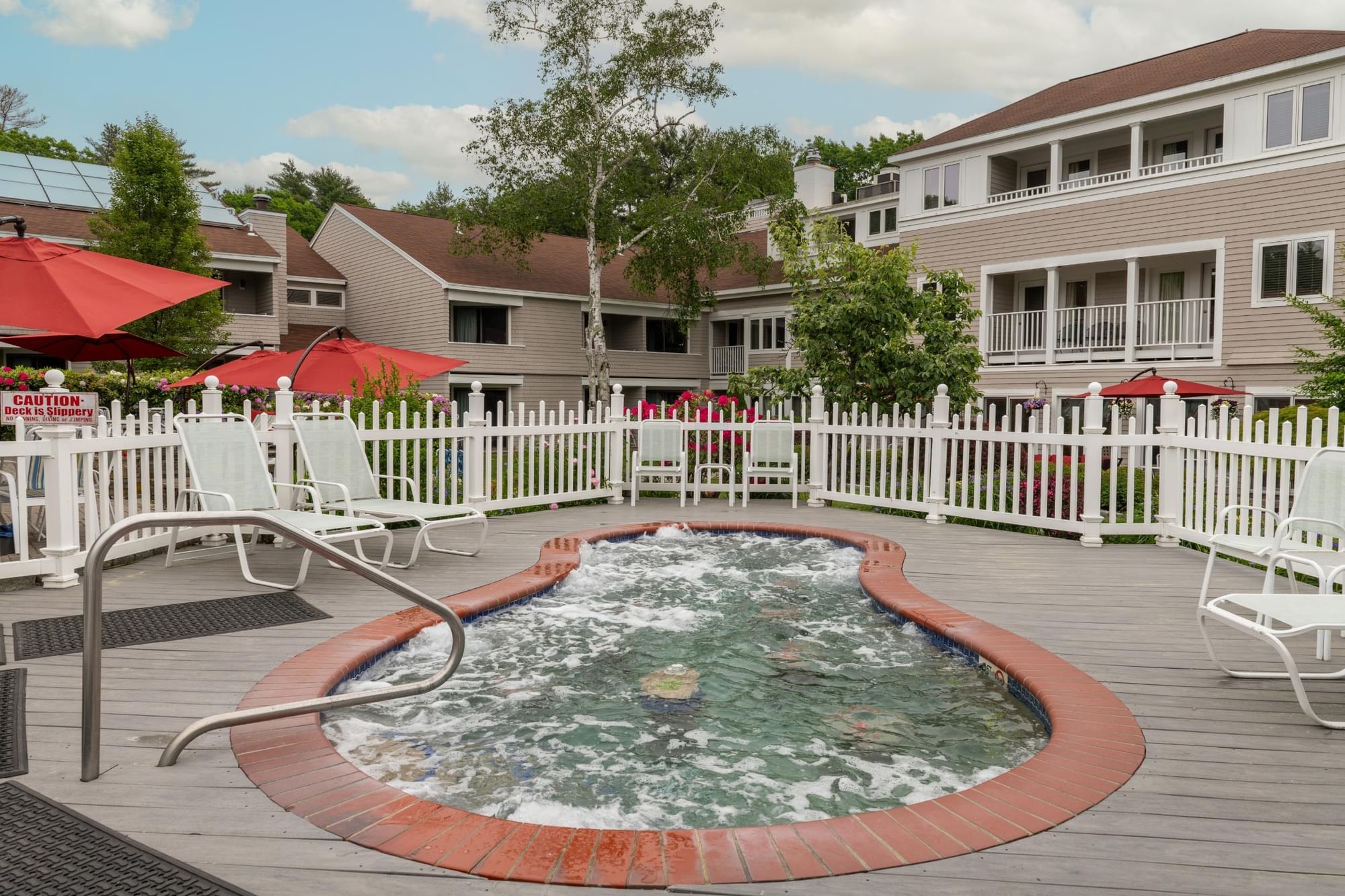 A hot tub with bubbles surrounded by white lounge chairs and red umbrellas on a deck.