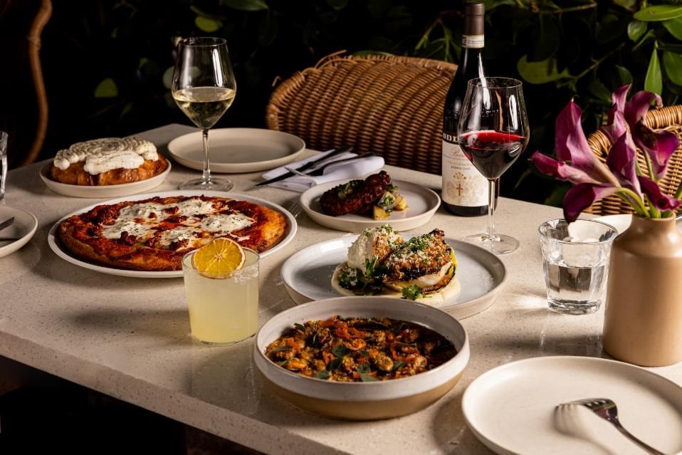 A table set with various dishes and glasses of wine and cocktails.
