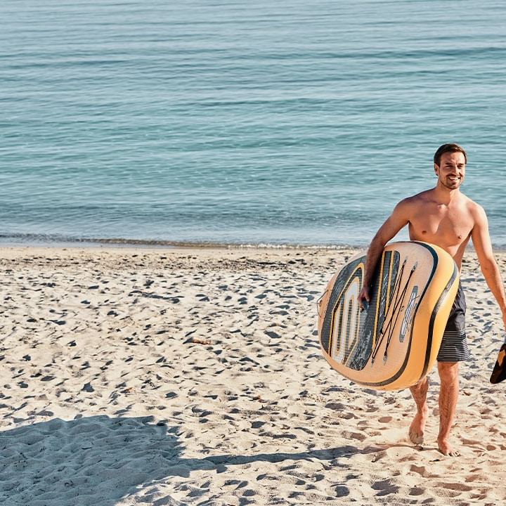 Uomo sulla spiaggia con una tavola da paddle e una pagaia, vicino all'acqua.