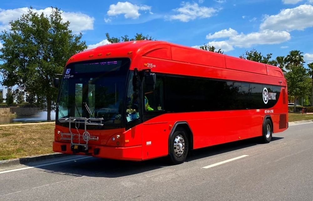 A red LYNX bus stopped on the side of the road with trees in the background.