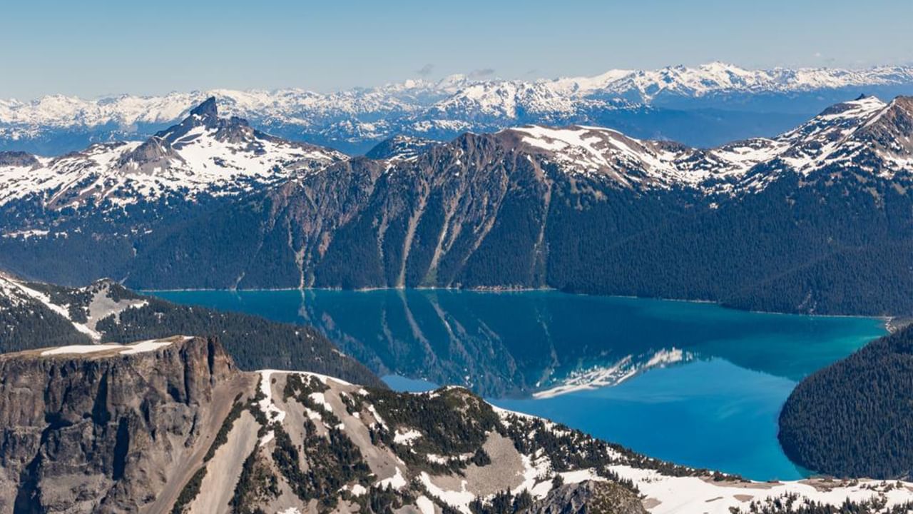 Panoramic view of turquoise lake surrounded by snowy mountains and forests at Harbour Air.