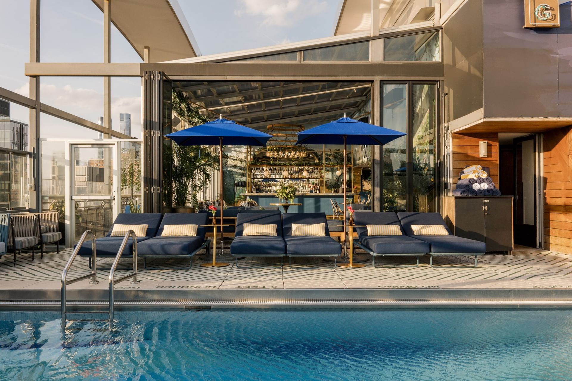 Rooftop pool with navy lounge chairs, blue umbrellas, and bar area at Gansevoort Meatpacking NYC
