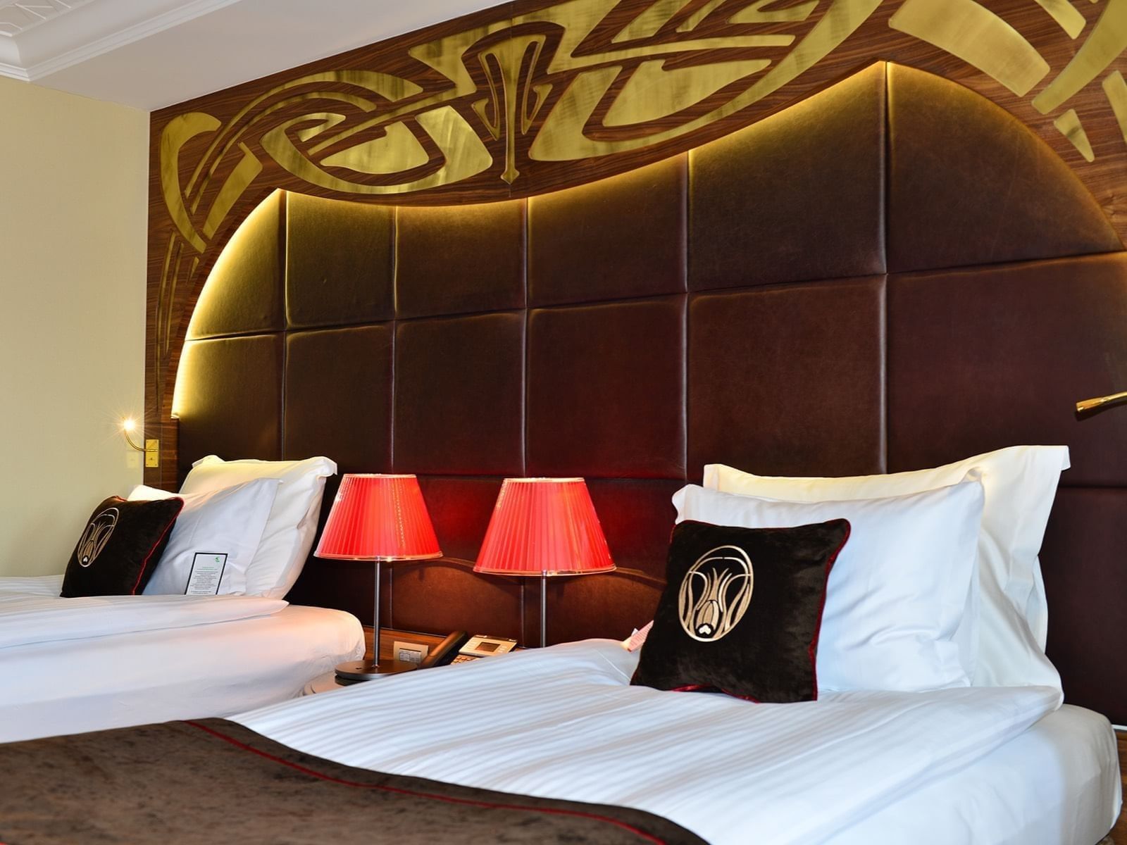 Red lamps by a padded headboard under a wooden arch surrounding twin beds in Deluxe Rooms at Warwick Ankara