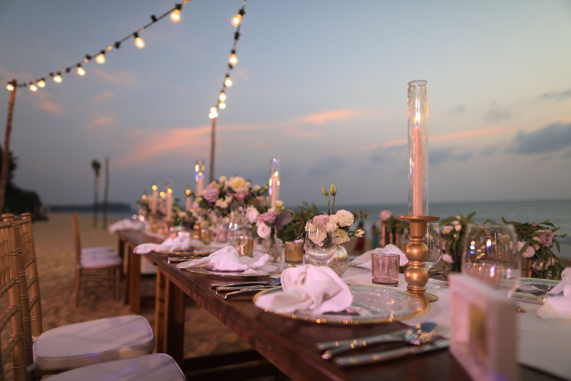 Elegant beach dining setup at sunset, with flowers, candles, and string lights at The Diplomat Resort