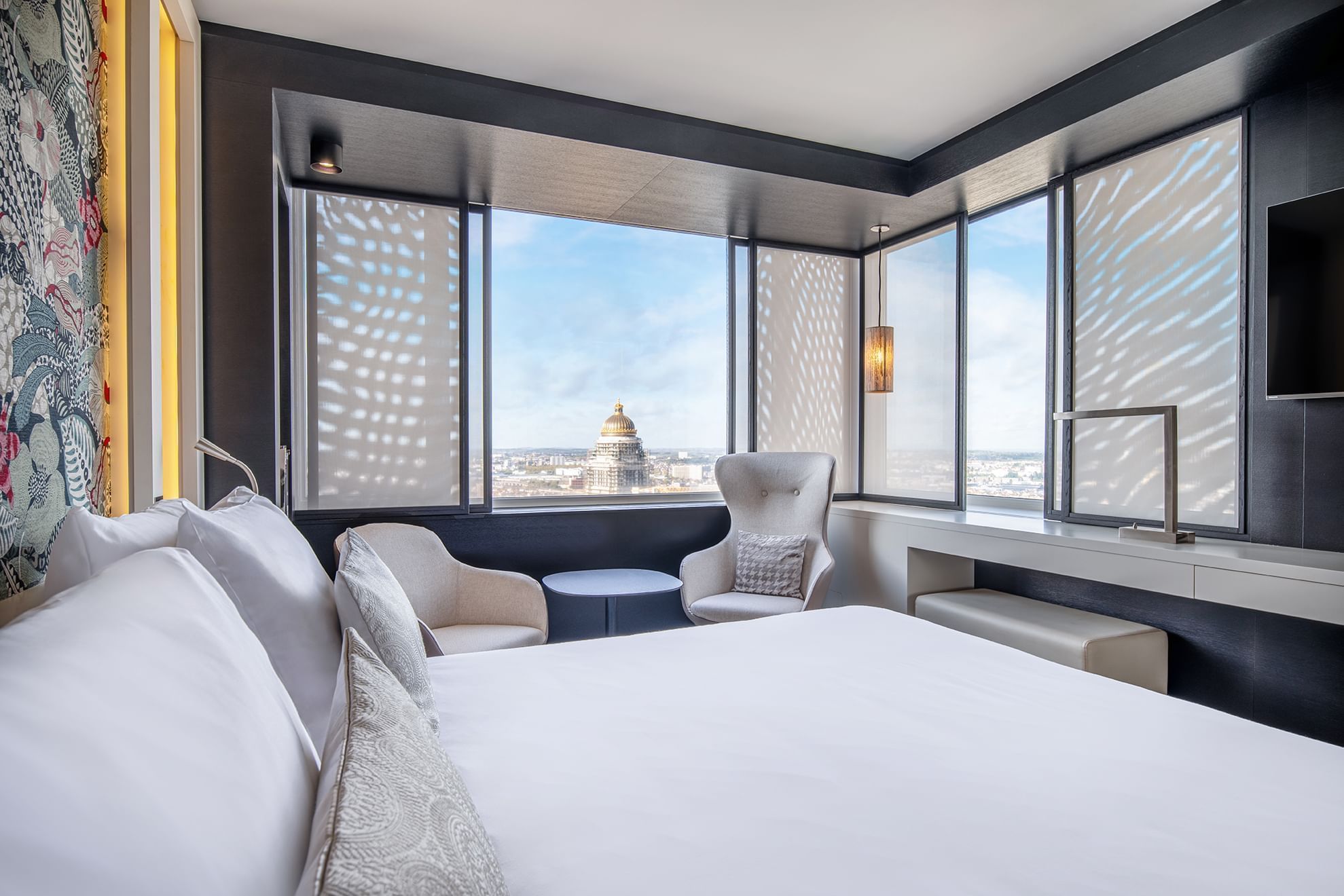 Interior of a modern hotel room with a comfy bed, TV & large windows at The Hotels Brussels