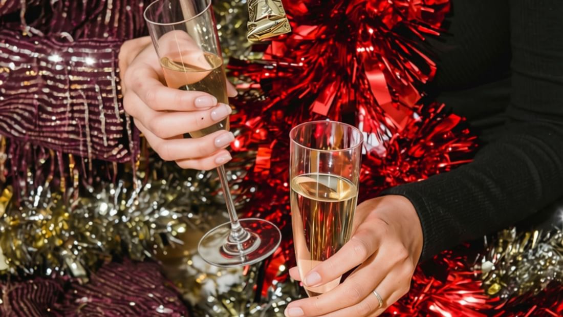 Two people in festive attire holding champagne glasses surrounded by red, gold, and silver metallic decorations.