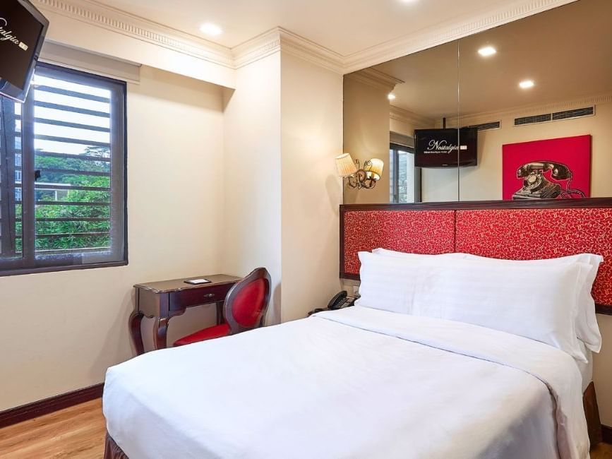 Large bed with comfy pillows & work desk in Deluxe Queen Room at Nostalgia Hotel Singapore