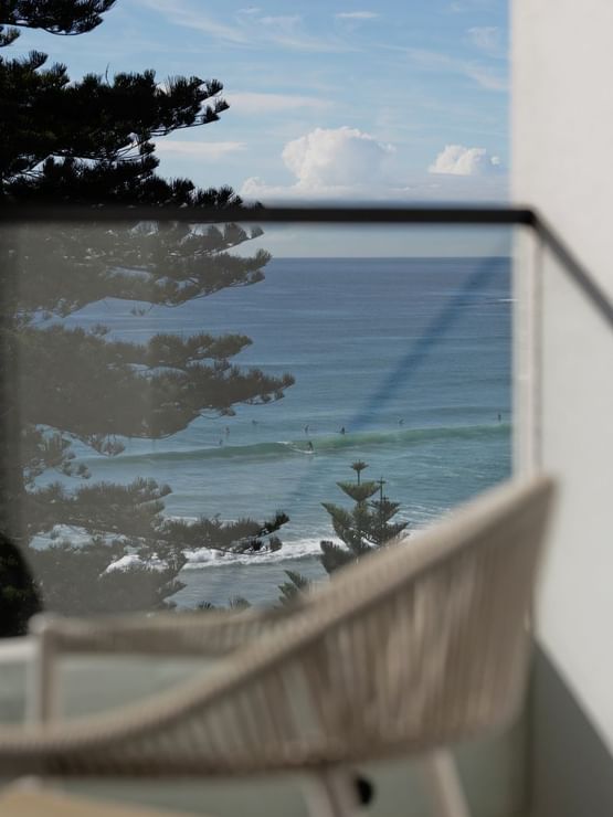 Coastal Two Bedroom Suite at Elysium Manly, featuring surfers on waves by pine trees, offering cozy Manly accommodation