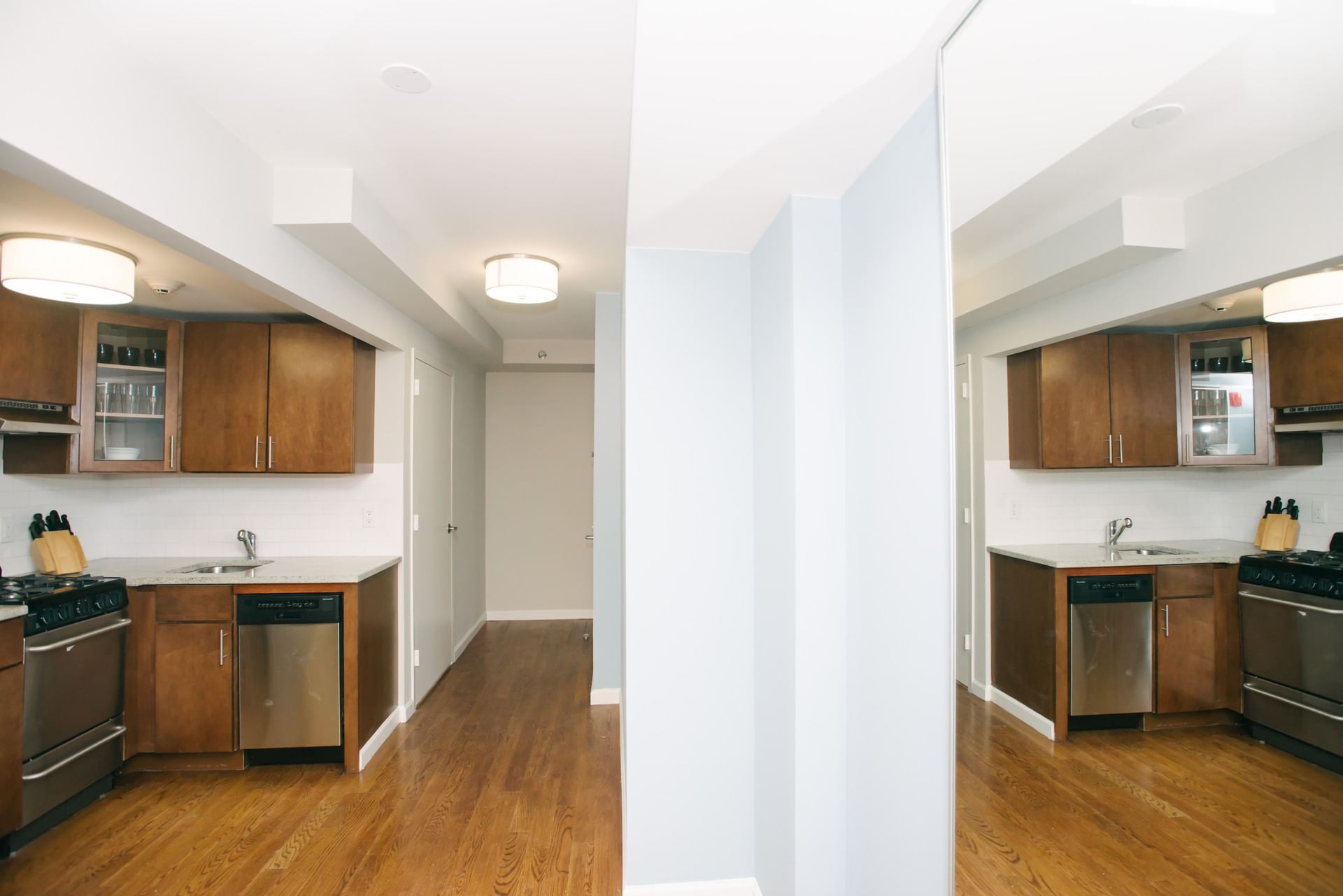 A wide view of a kitchenette with wooden cabinets, stainless steel appliances, and hardwood flooring.