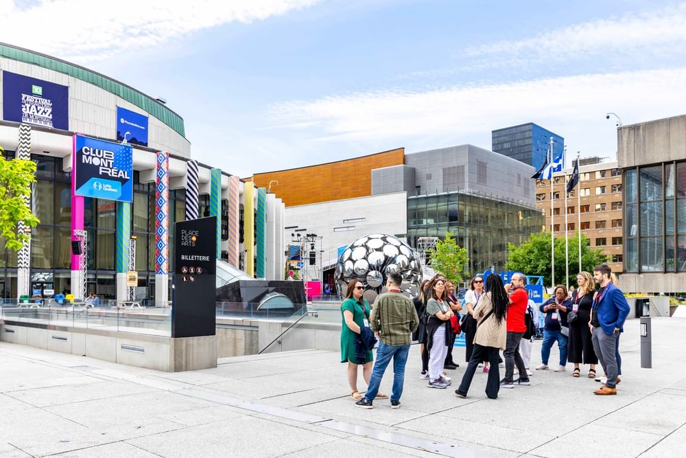 Visitors gather in a modern urban plaza with contemporary buildings and a large soccer ball sculpture at Warwick Le Crystal Montreal
