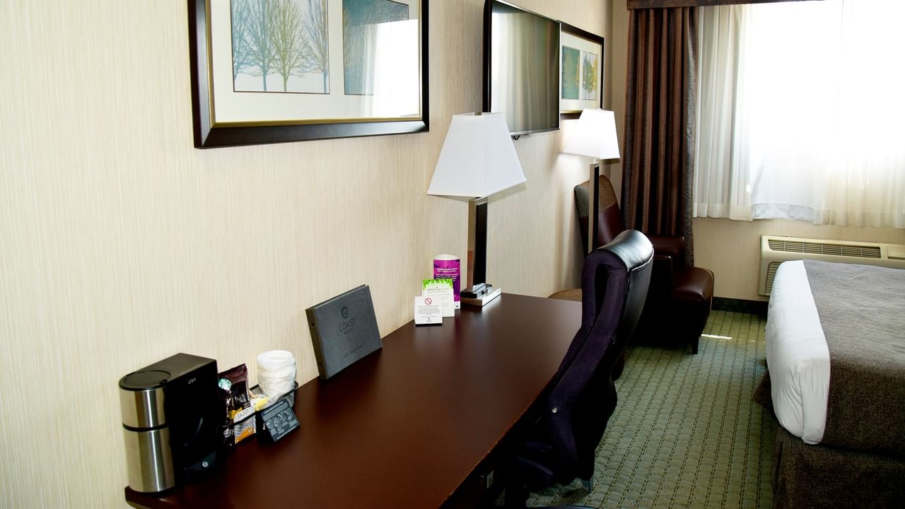 A hotel room with a desk, chair, bed, and two framed pictures on the wall.