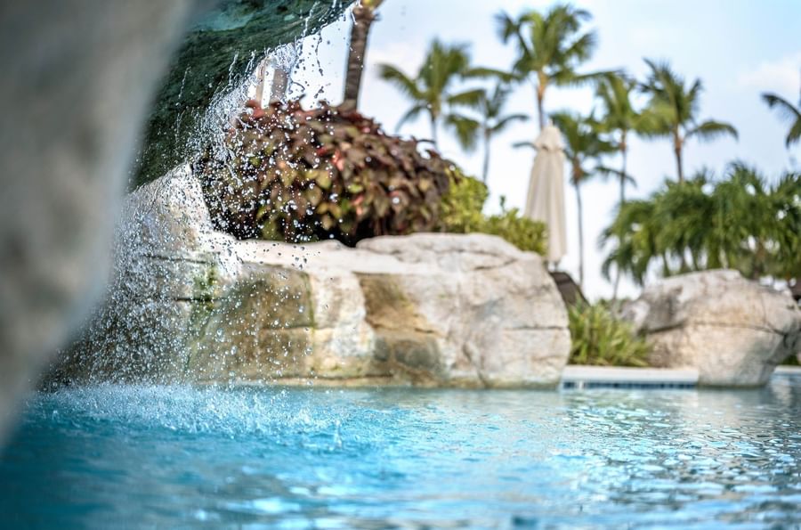 Water cascading by large rocks into a clear pool surrounding tropical palm trees at Warwick Paradise Island Bahamas