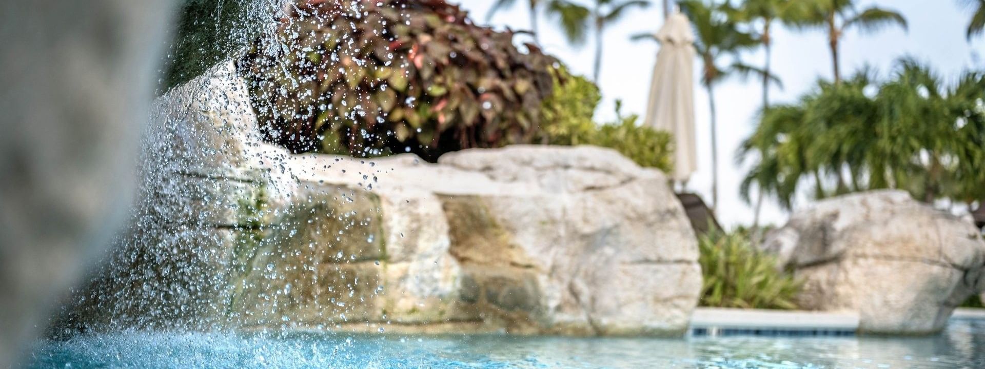 Water cascading by large rocks into a clear pool surrounding tropical palm trees at Warwick Paradise Island Bahamas