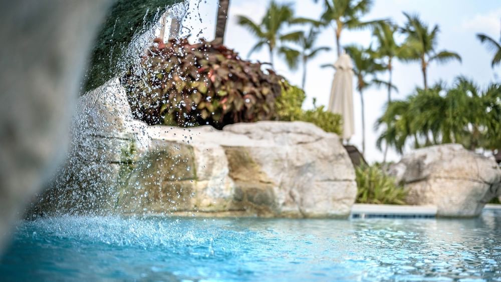 Water cascading by large rocks into a clear pool surrounding tropical palm trees at Warwick Paradise Island Bahamas