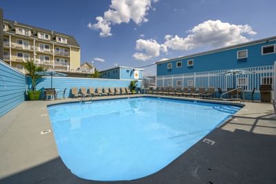 Pool area surrounded by blue walls and lounge chairs, with a clear sky and fluffy clouds above at Madison Beach Motel