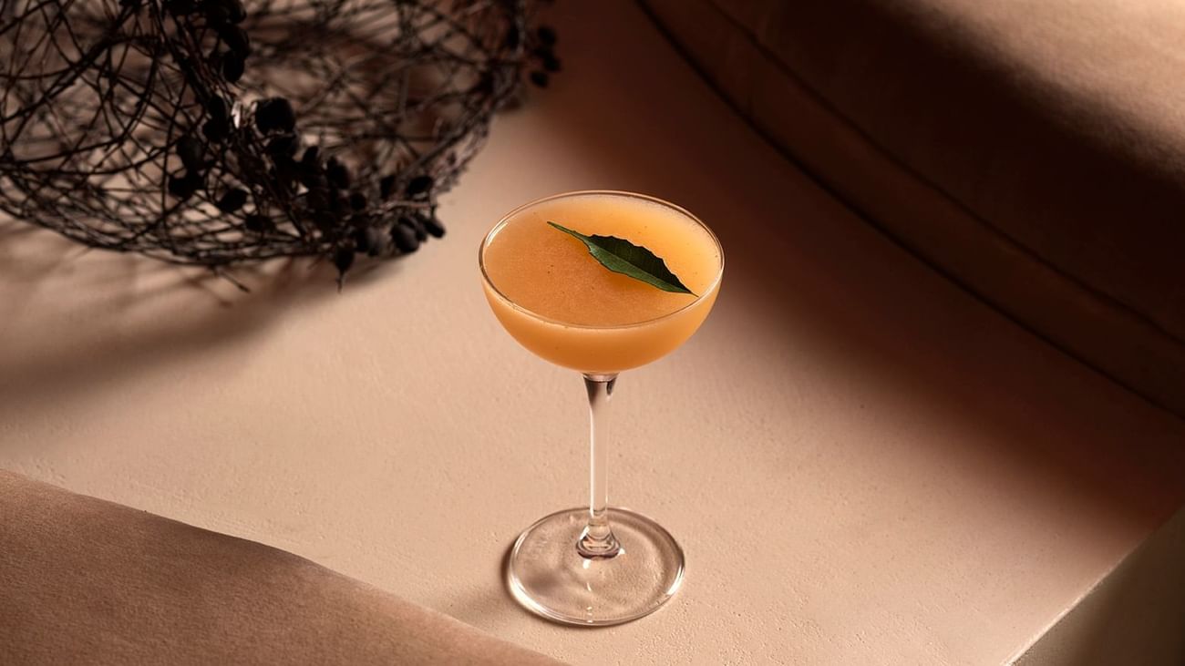 Cocktail with a leaf garnish on a couch, with a decorative metal basket nearby.