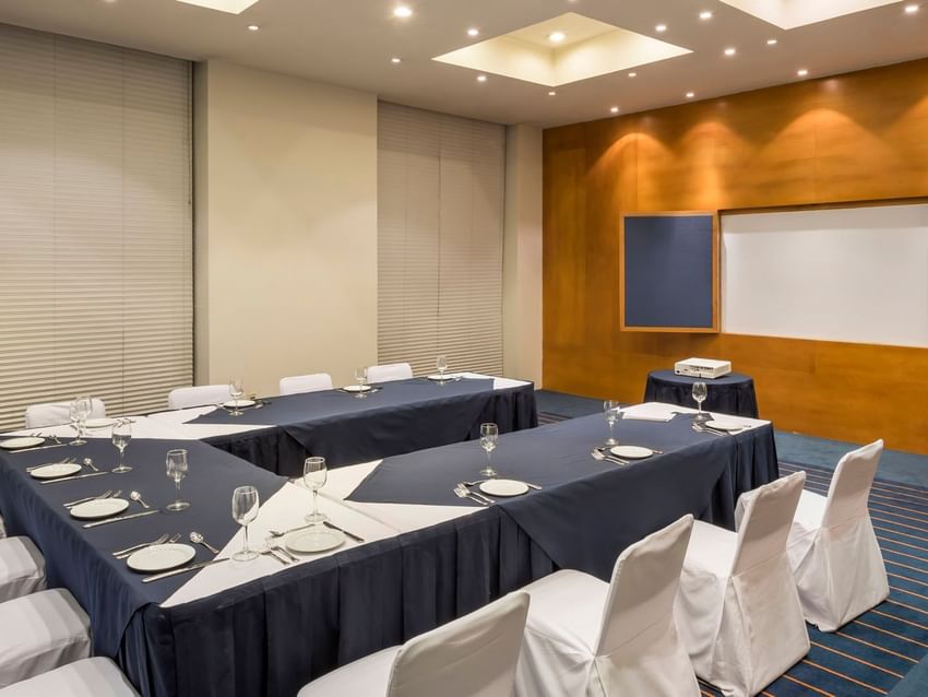 U-shaped table setup with a projector screen and carpeted floors in the Londres Venue at Real Inn San Luis Potosi