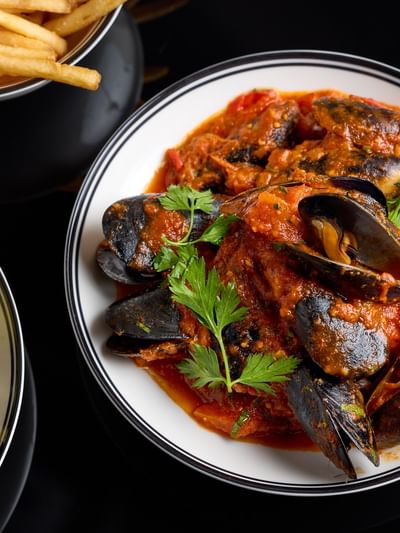 Plate of mussels in sauce with fries on the side as an offer.