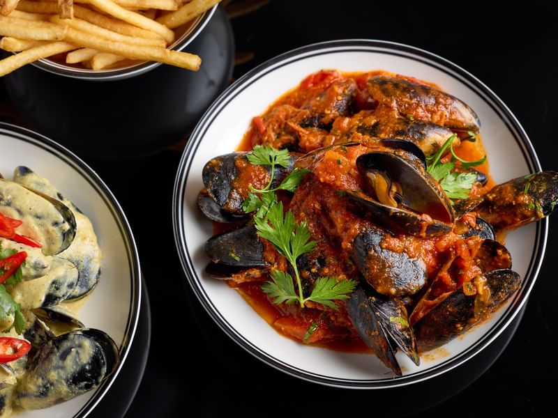 Plate of mussels in sauce with fries on the side as an offer.