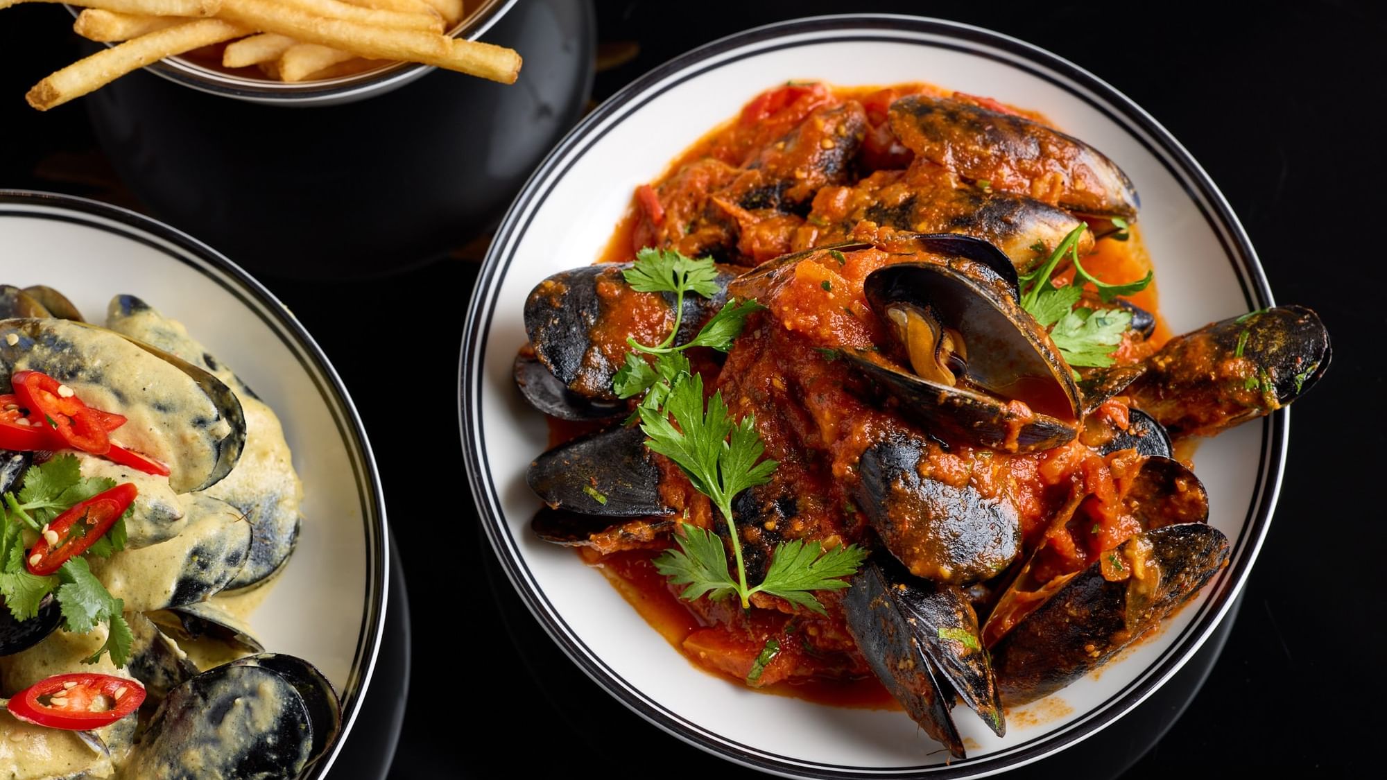Plate of mussels in sauce with fries on the side as an offer.