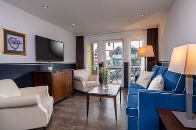 Living room with couch, chairs, coffee table, TV, and balcony access in a cozy, modern setting.