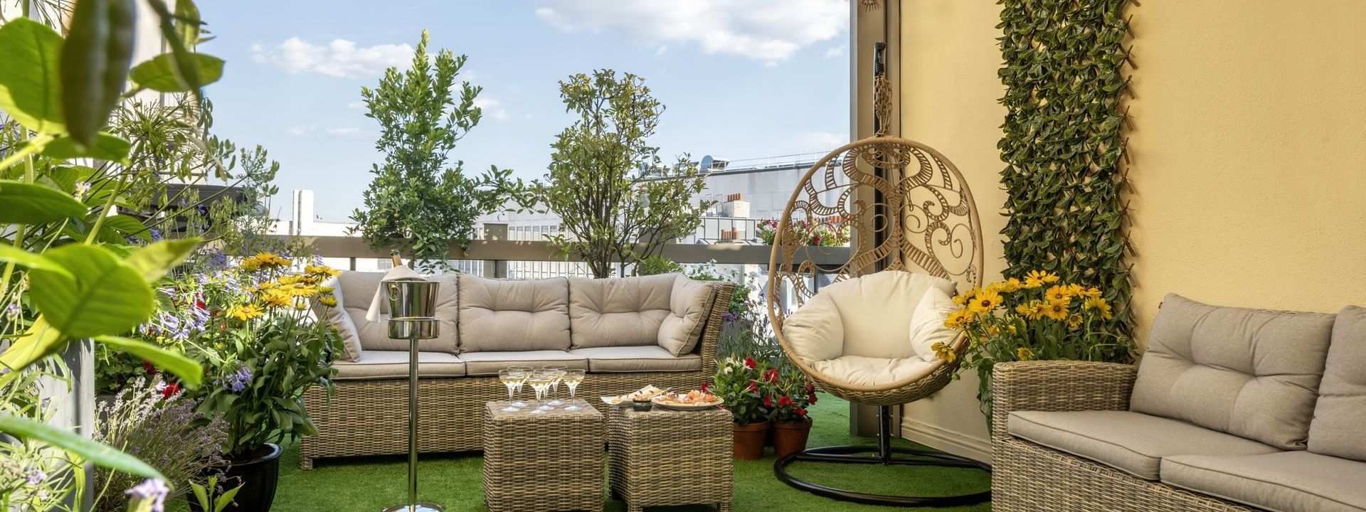 Terrasse ensoleillée avec mobilier en rotin, végétation luxuriante et fauteuil suspendu au Warwick Paris Champs-Elysées