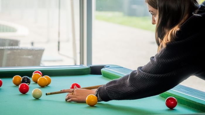 A lady playing billiard in a game room at The Originals Hotels