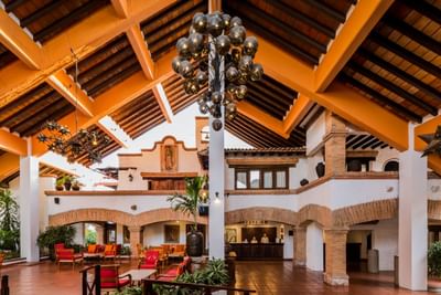 Interior of hotel lobby with brick arches, red chairs, and large decorative chandelier hanging from wooden ceiling.