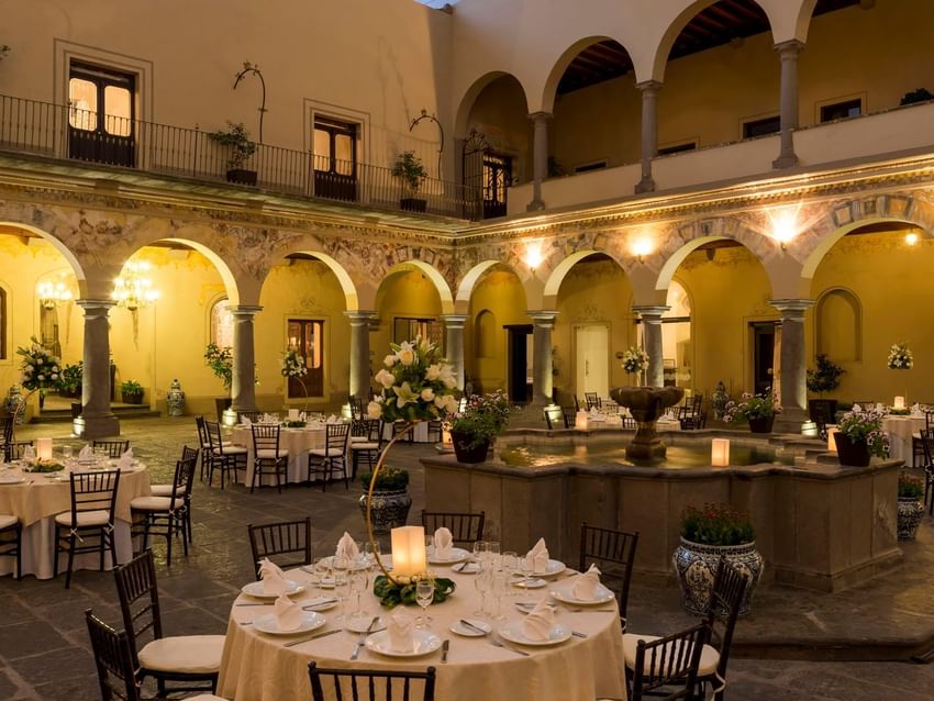 Evening banquet in a stone courtyard with a central fountain and lit colonial arches in Patio Novicias at Quinta Real Puebla