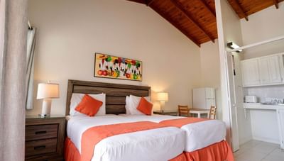 Beds with orange accents below colorful painting and under a high wooden ceiling in Standard Room at Worthing Court Apartment