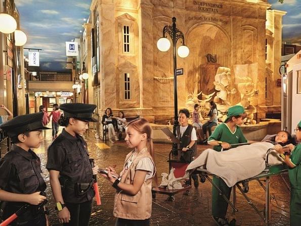 Kids dressed as police officers and medical staff, with fountain backdrop in Kidzania near Saujana Hotel Kuala Lumpur