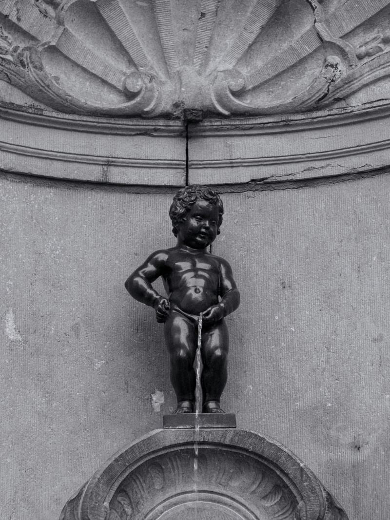 Black and white photo of the Manneken Pis statue by a stone wall under a ledge at Hotel Barsey by Warwick
