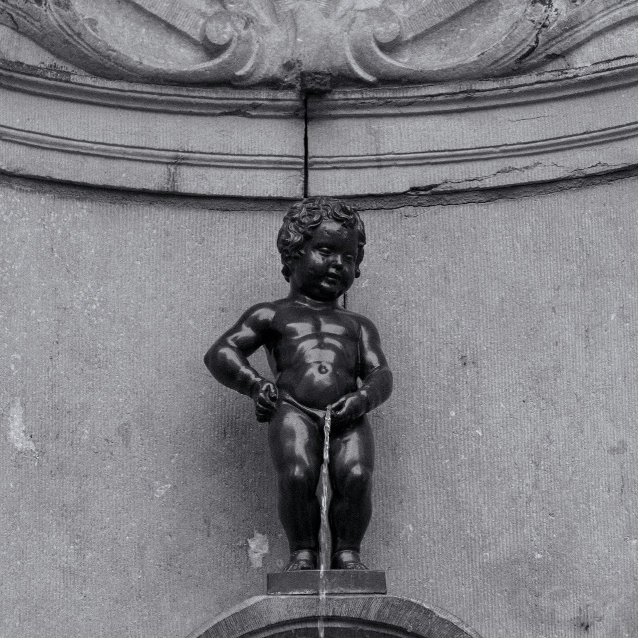Black and white photo of the Manneken Pis statue by a stone wall under a ledge at Hotel Barsey by Warwick