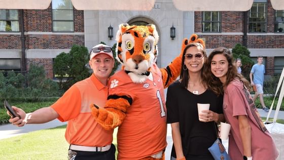 Happy family smiling and posing together with a friendly mascot tiger outdoors at Clemson University Conference Center & Inn