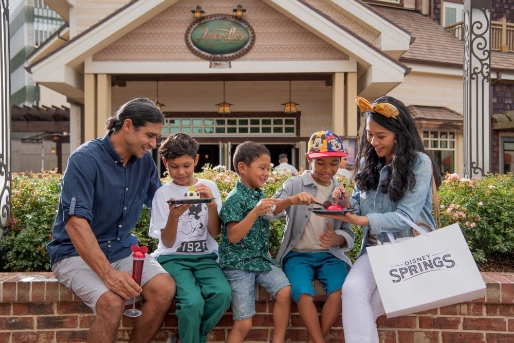 A mom and dad share treats with three boy sitting on a brick wall in front of Amorette's at Disney Springs.