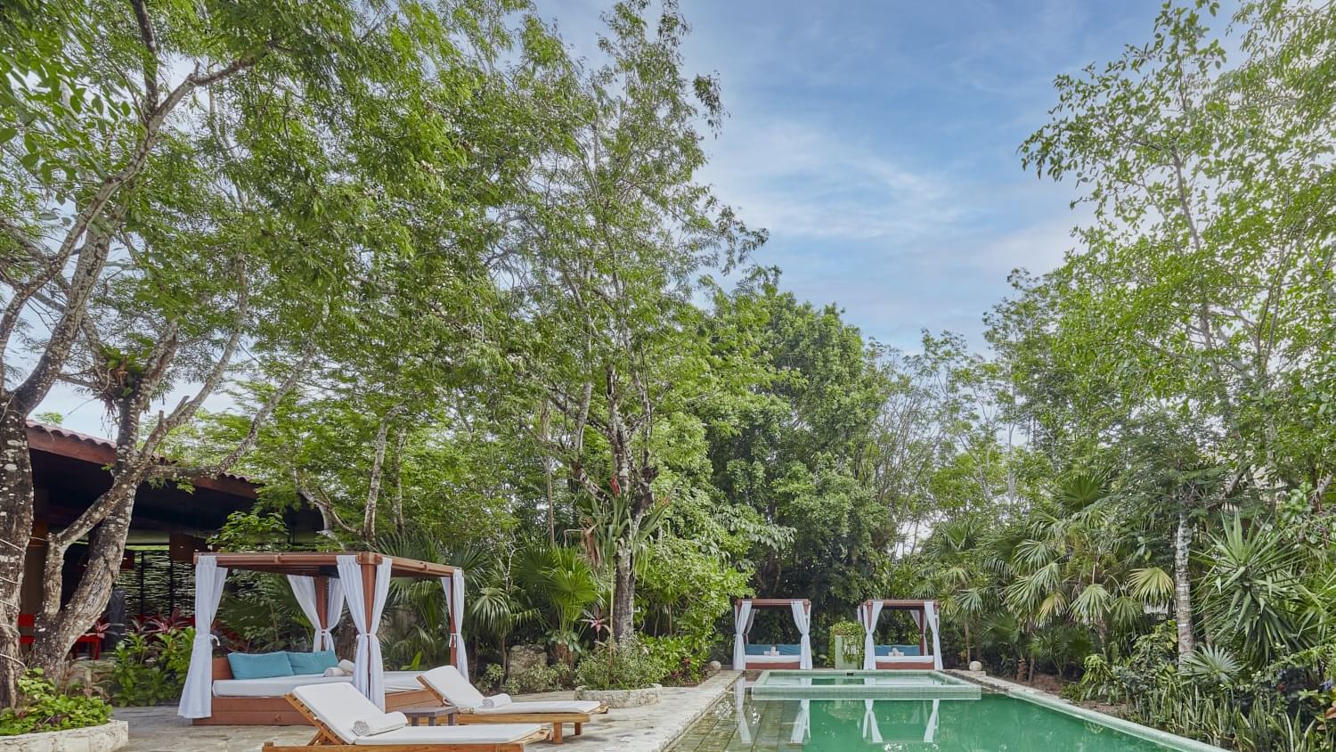 Canopy beds and sun loungers by the outdoor pool with lush greenery at The Explorean Cozumel