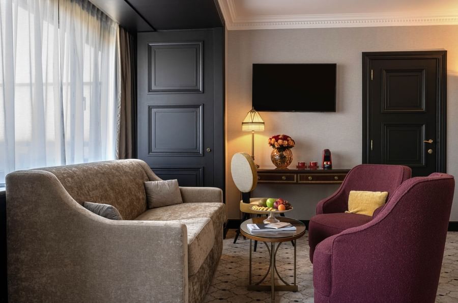 Beige sofa by a black door and red armchairs surrounding a glass table under a TV in Junior Suite at Hotel Barsey by Warwick