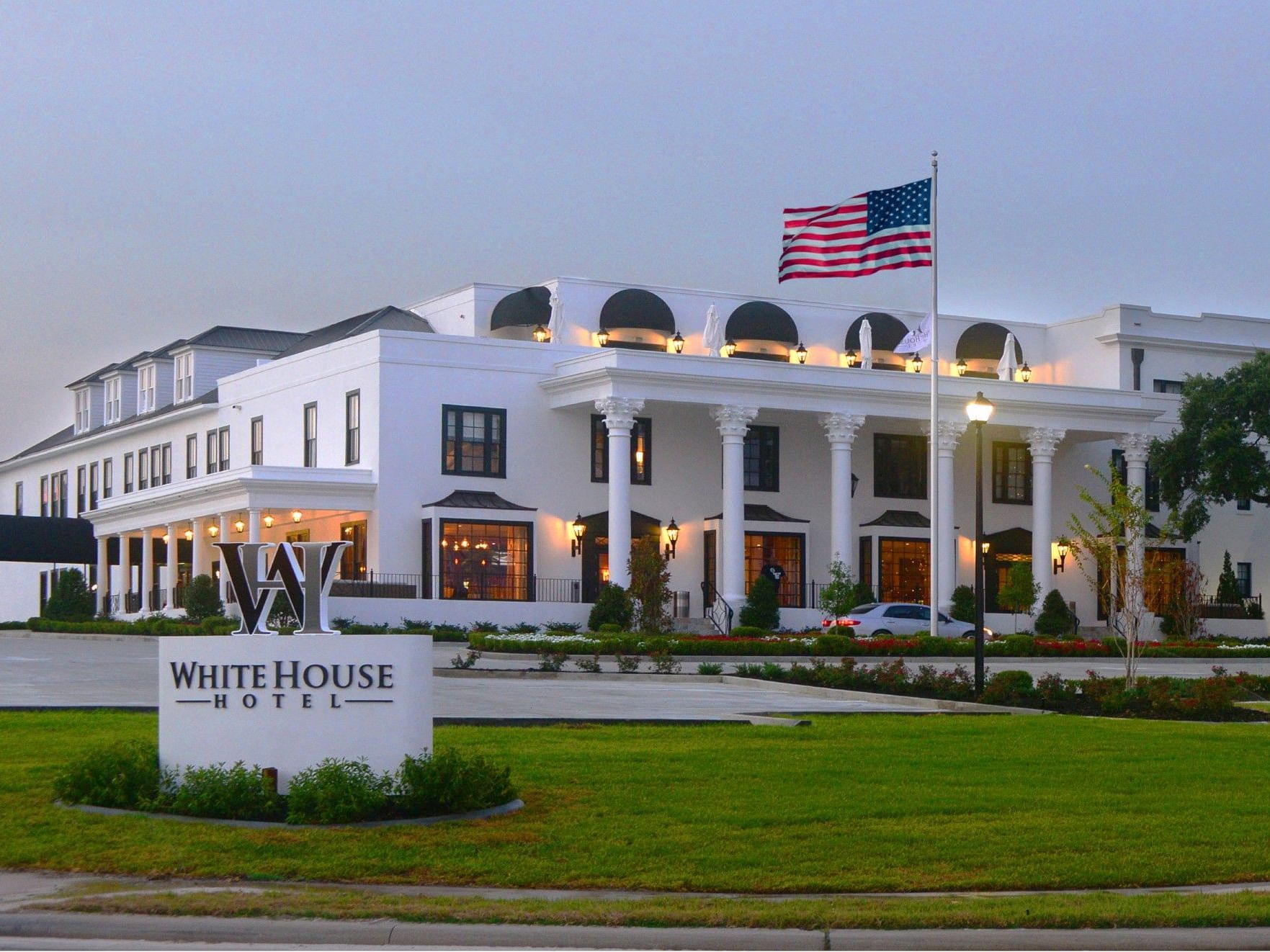 Exterior view of The White House Hotel, with white columns and an American flag on a sunny day
