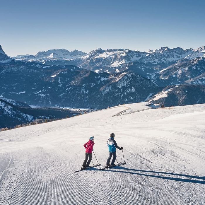 Zwei Skifahrer auf einem schneebedeckten Berghang vor einer majestätischen Bergkulisse.