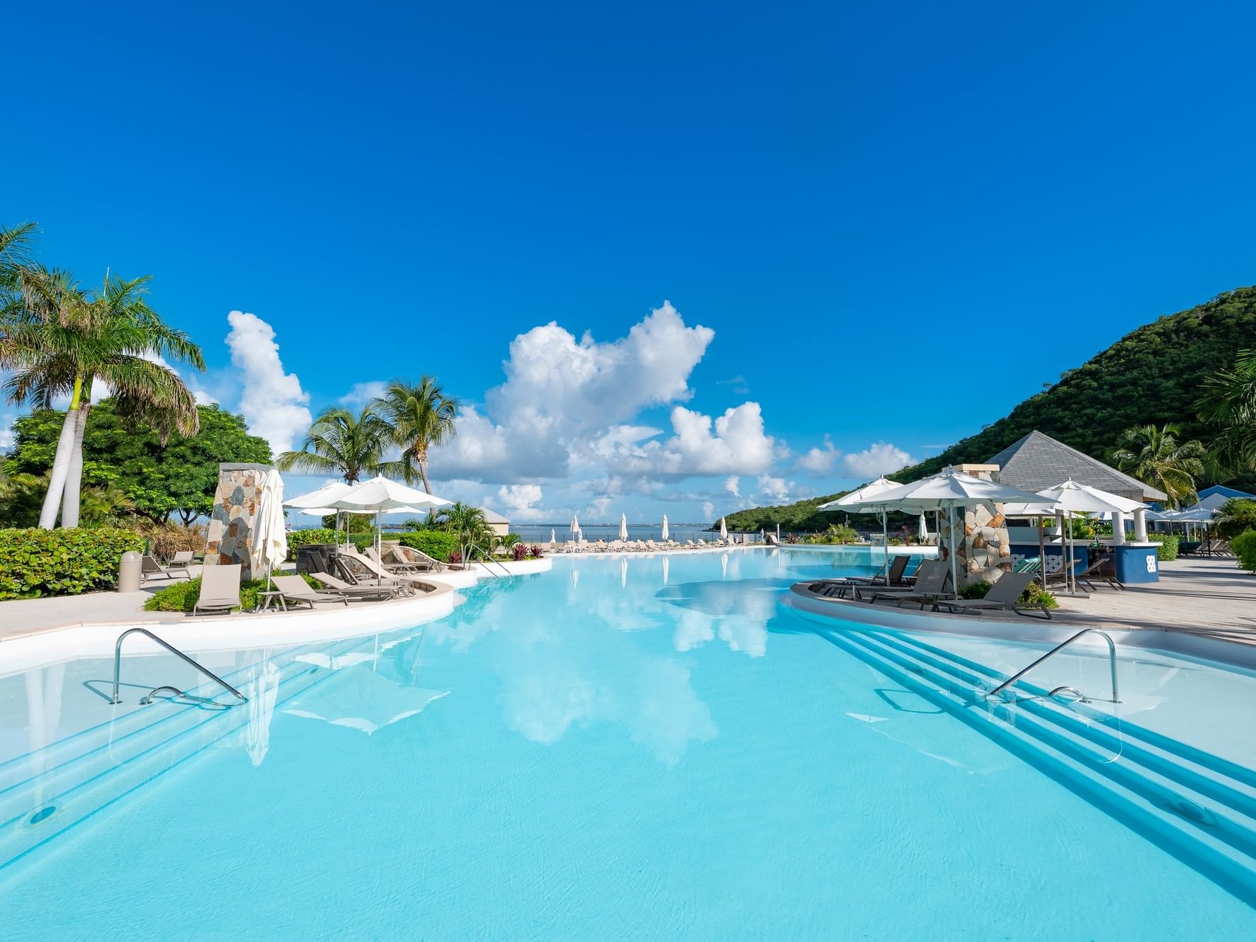 Outdoor pool and Sugar Reef Poolside Bar at Saint Martin Beach Resort & Spa with blue sky, clouds, and greenery