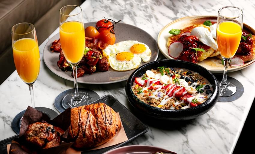 Three plates with different breakfast meals and three glasses of orange juice at Paradox Vancouver